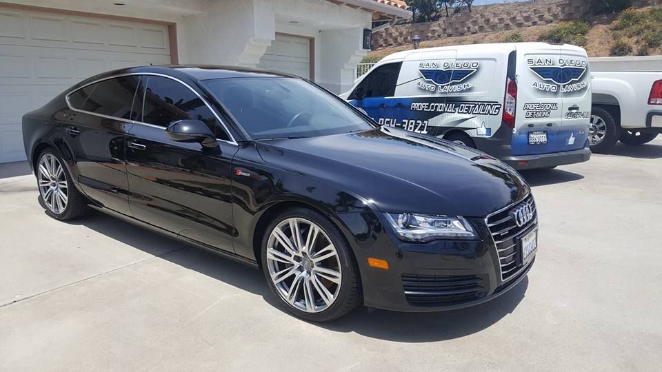 A black audi a7 is parked in front of a garage next to a white van.