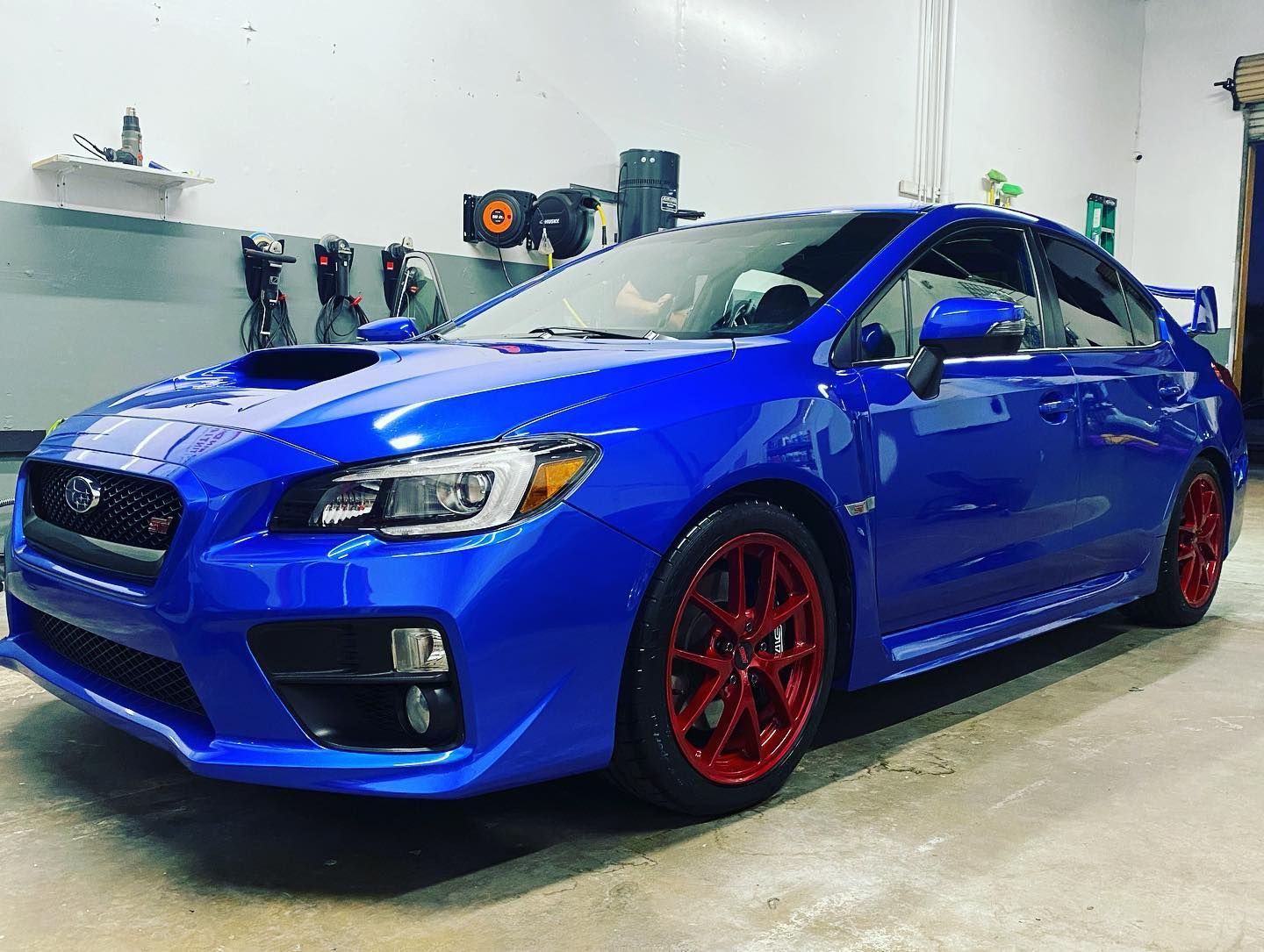 A blue subaru wrx sti with red wheels is parked in a garage.