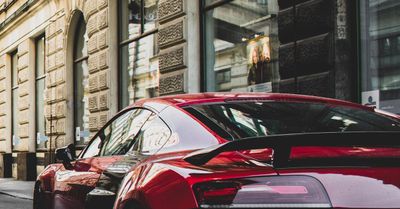 A red sports car is parked on the side of the road in front of a building.