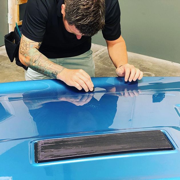 A man is working on the hood of a blue car