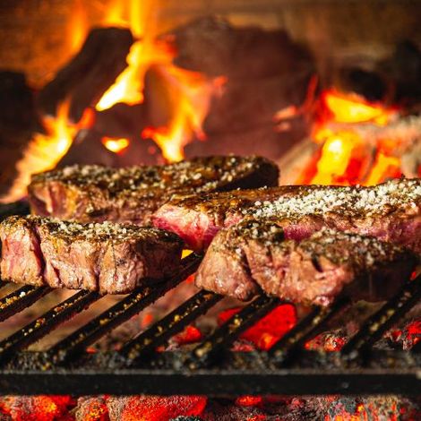 Steaks are cooking on a grill over a fire.