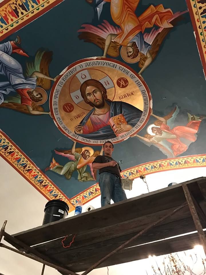 A man is standing on a scaffolding in front of a painting of jesus on the ceiling.