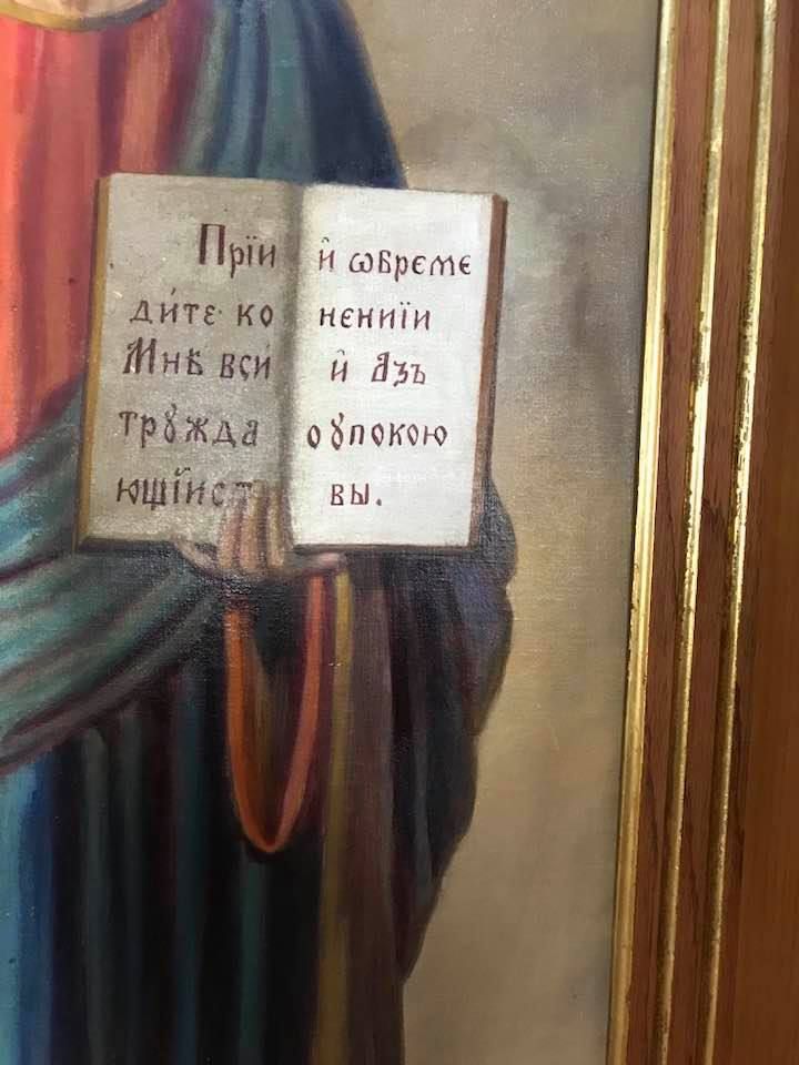 A painting of jesus holding a book with russian writing on it.