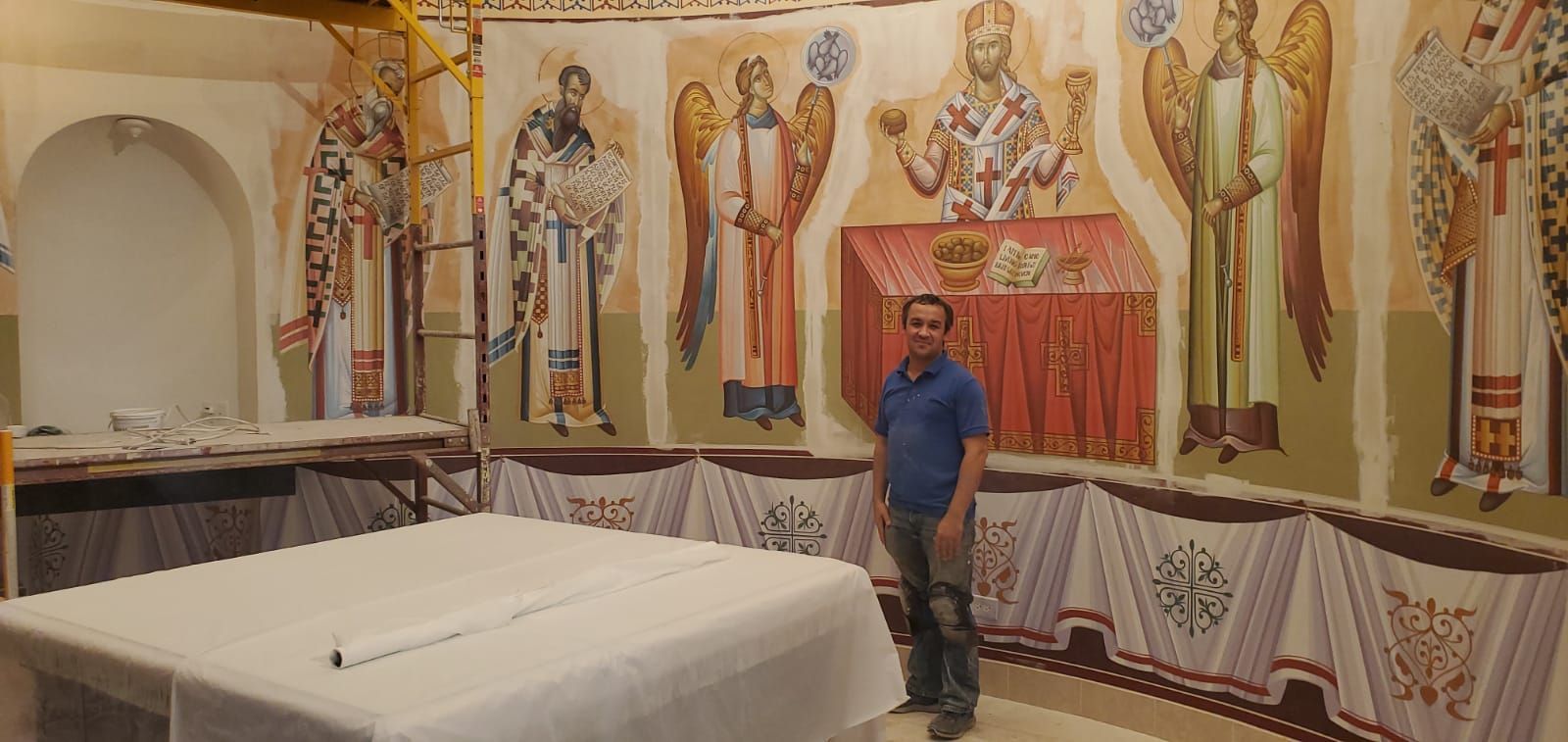 A man is standing in front of a painting on the wall of a church.