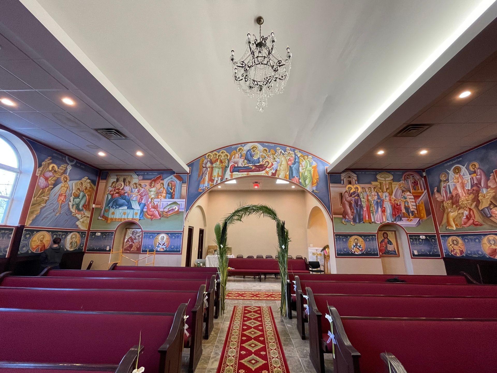 The inside of a church with red benches and a chandelier hanging from the ceiling.