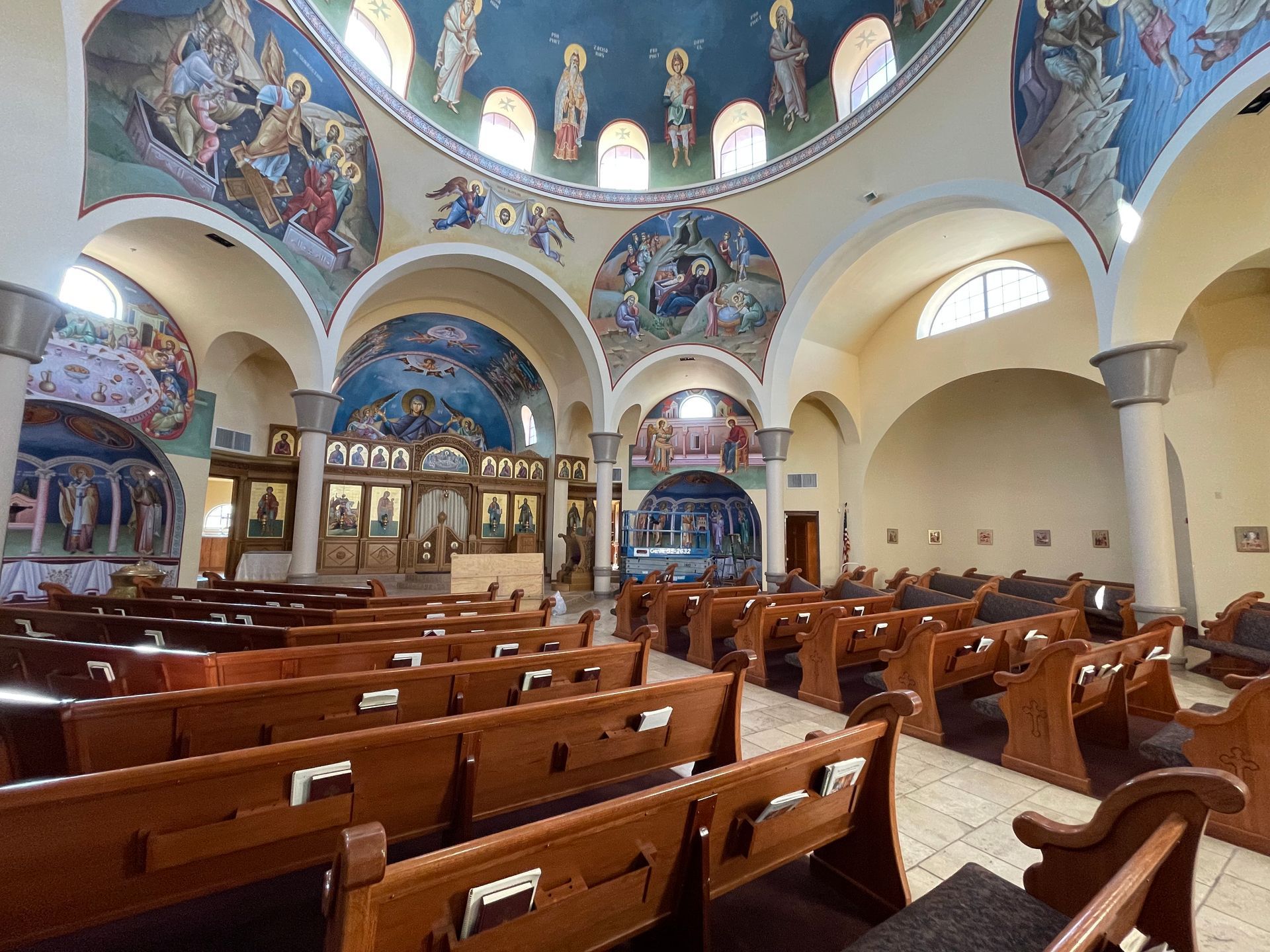 The inside of a church with rows of wooden benches and paintings on the ceiling.