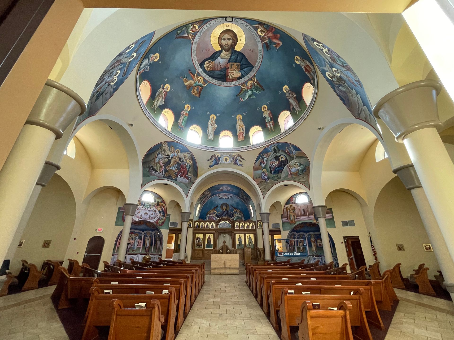 The inside of a church with rows of wooden benches and a dome.