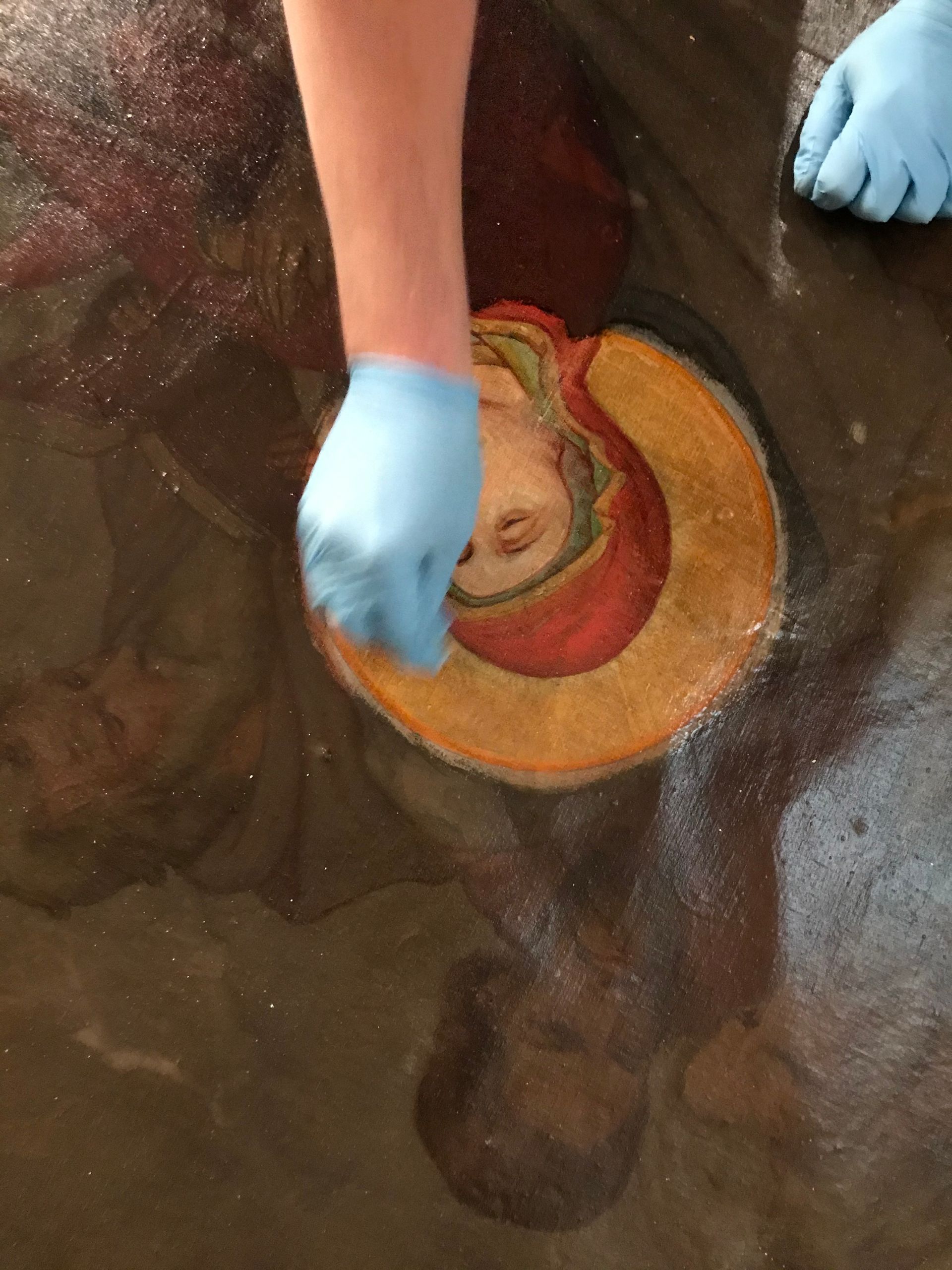 A person wearing blue gloves is cleaning a painting