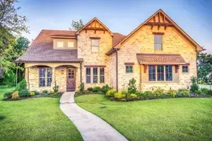 A large brick house with a lush green lawn and a walkway leading to it.