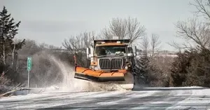 A snow plow is driving down a snow covered road.