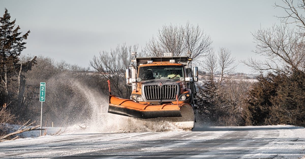 A snow plow is driving down a snow covered road.