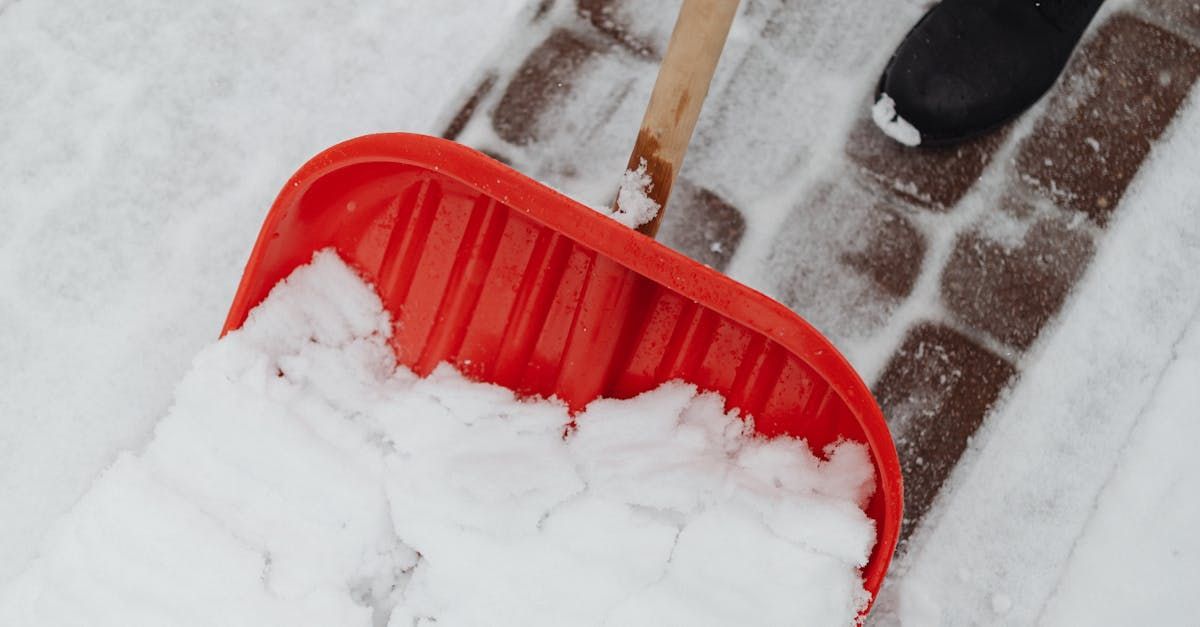 A person is shoveling snow from a sidewalk with a red shovel.
