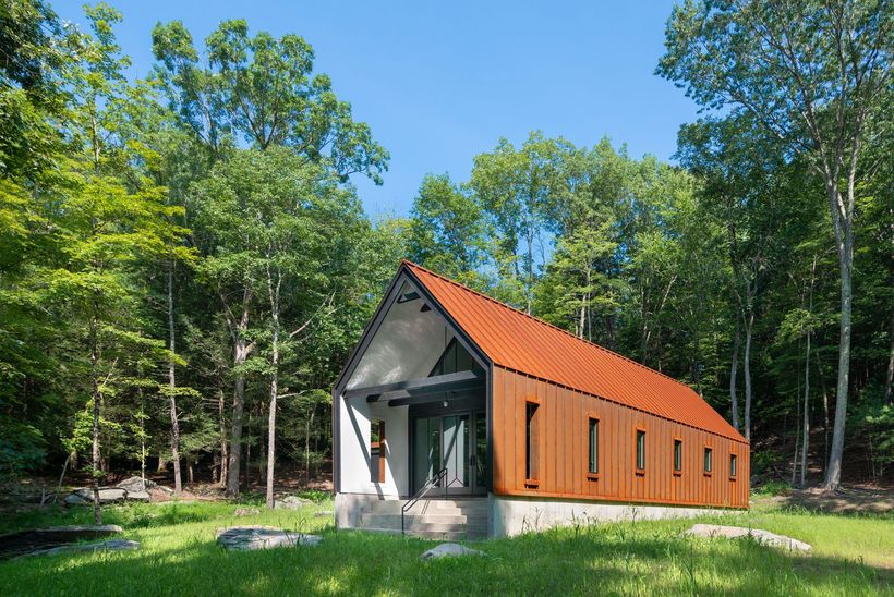 A small house with a red roof is in the middle of a forest.