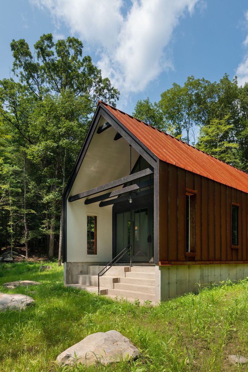 A small house with a red roof is surrounded by trees and grass.