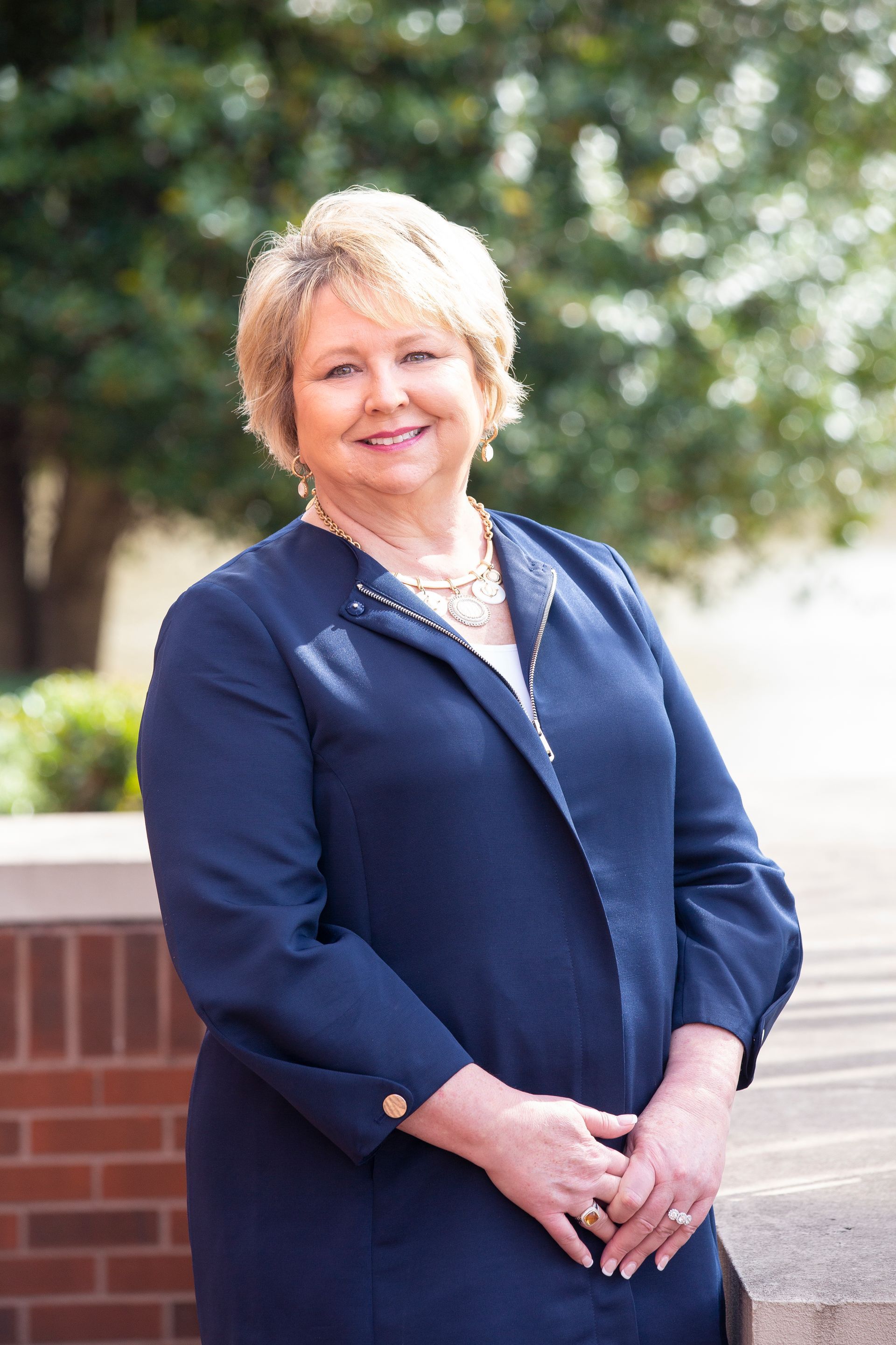 Woman with blonde hair in a blue blazer smiling outdoors.
