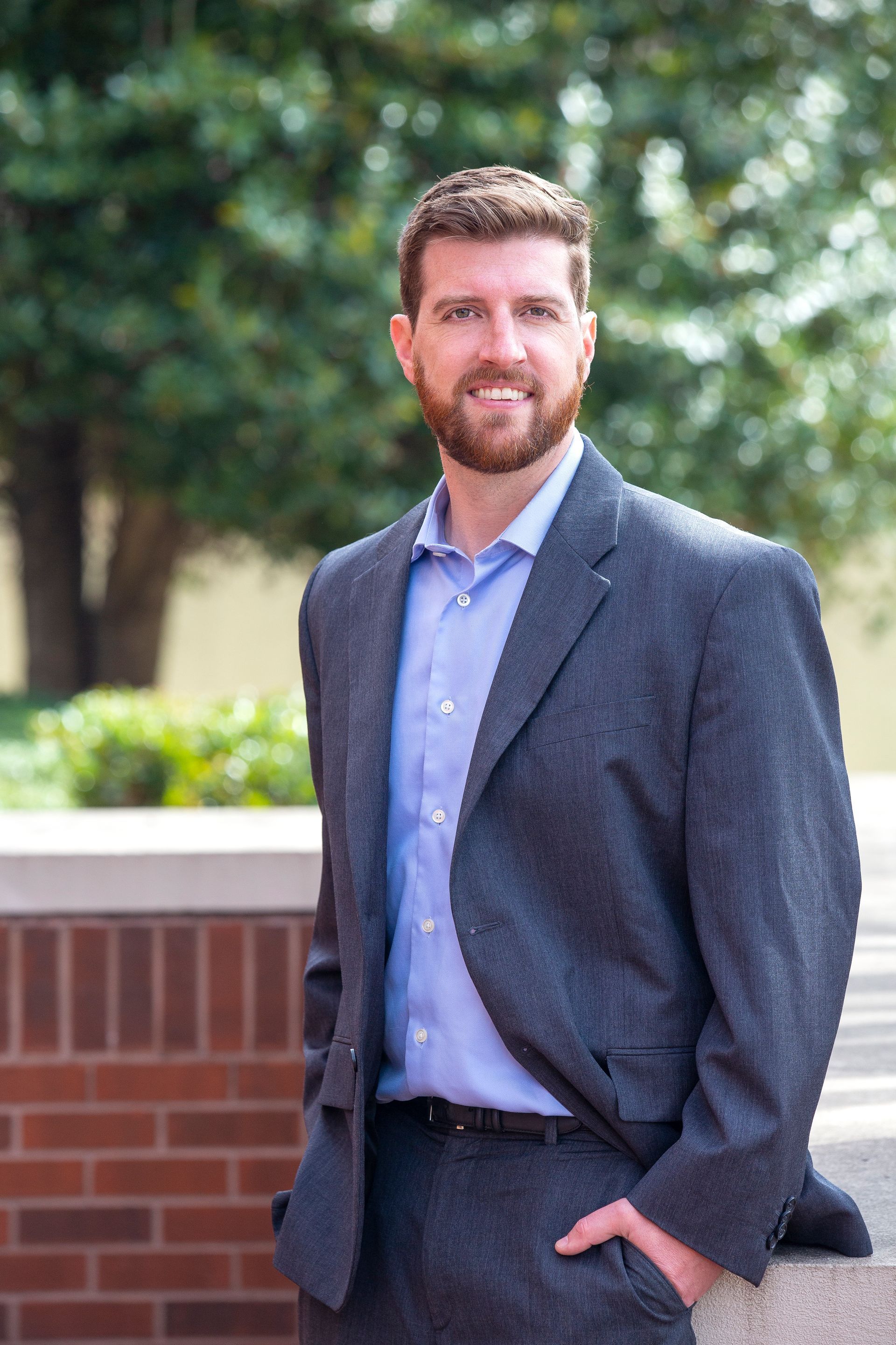 Man in suit, smiles, stands outdoors.
