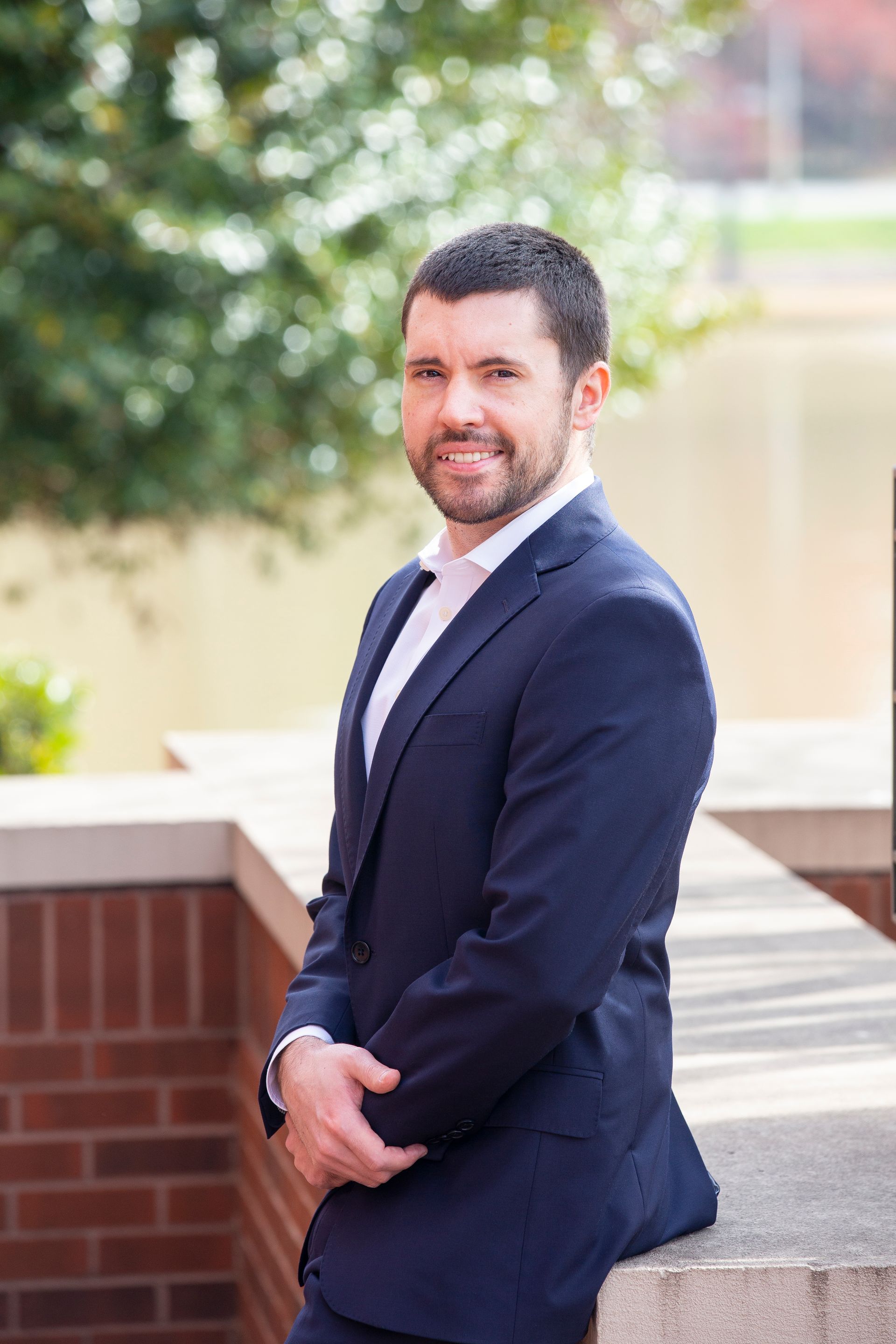 Man in a blue suit and white shirt smiling outdoors.