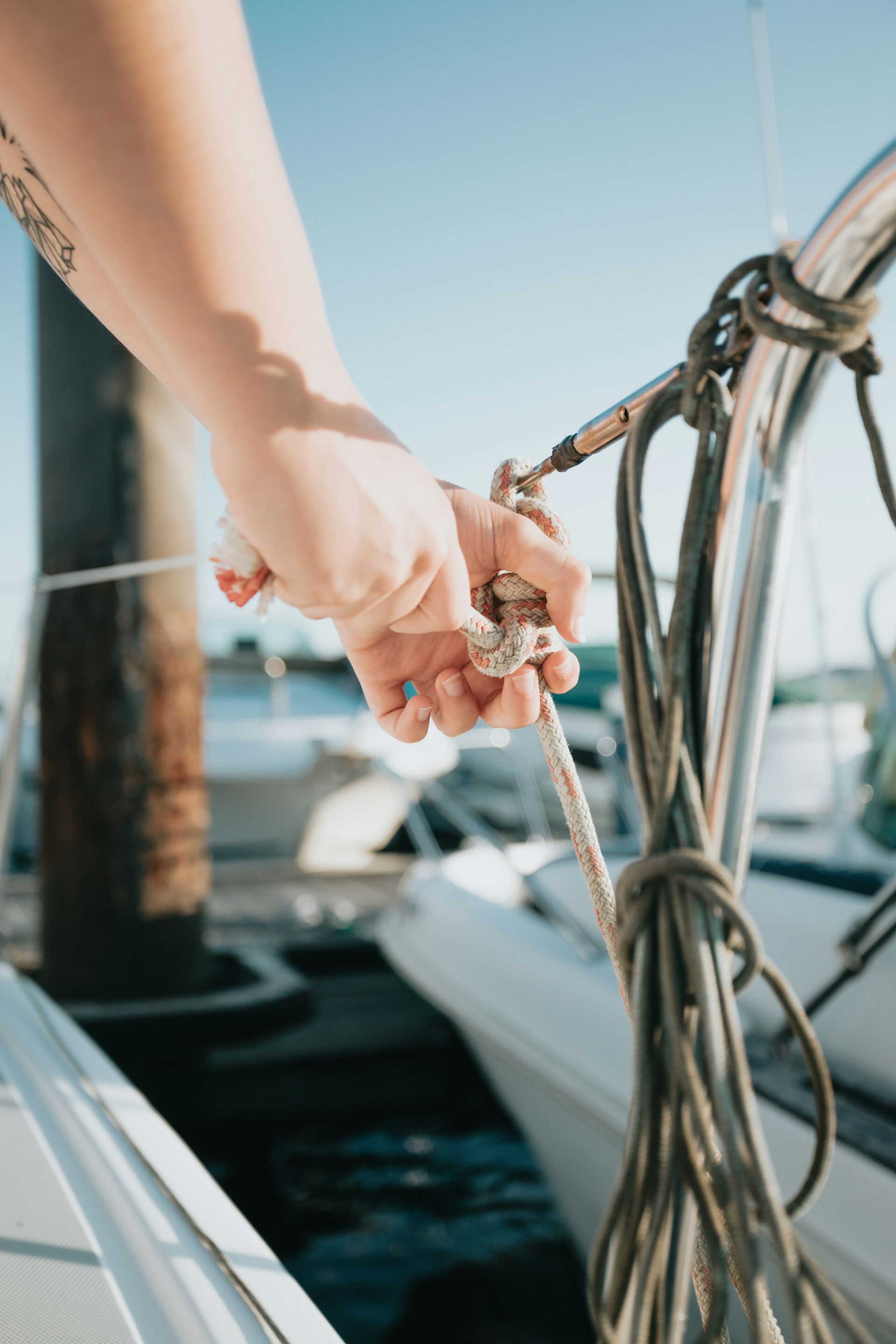Hand holding a rope on a boat, blue sky in the background.