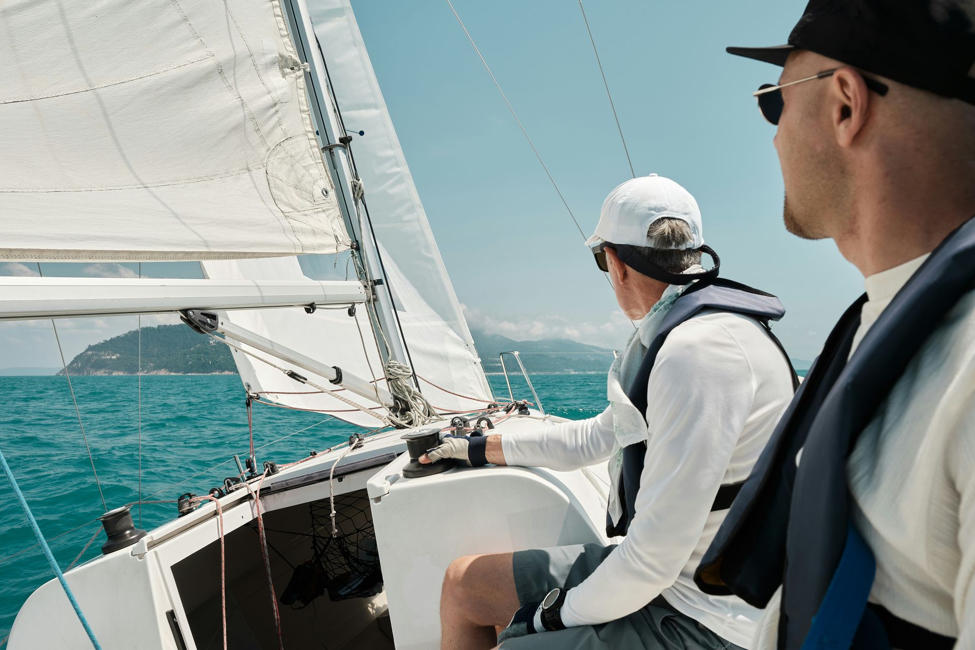 Two men sailing on a yacht, turquoise water, sunny day.