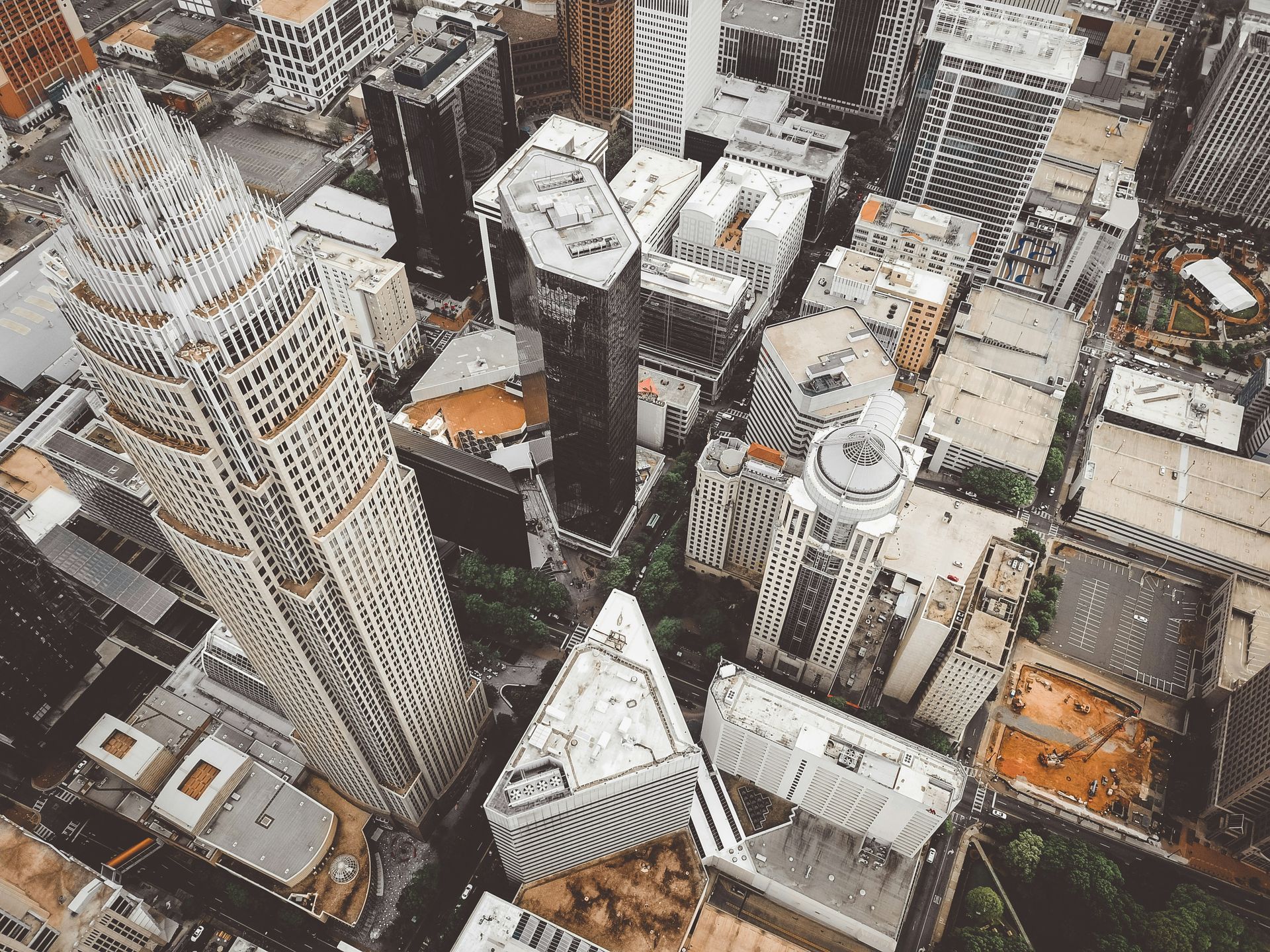 Aerial view of a city with tall buildings, some with unique shapes, in neutral colors.