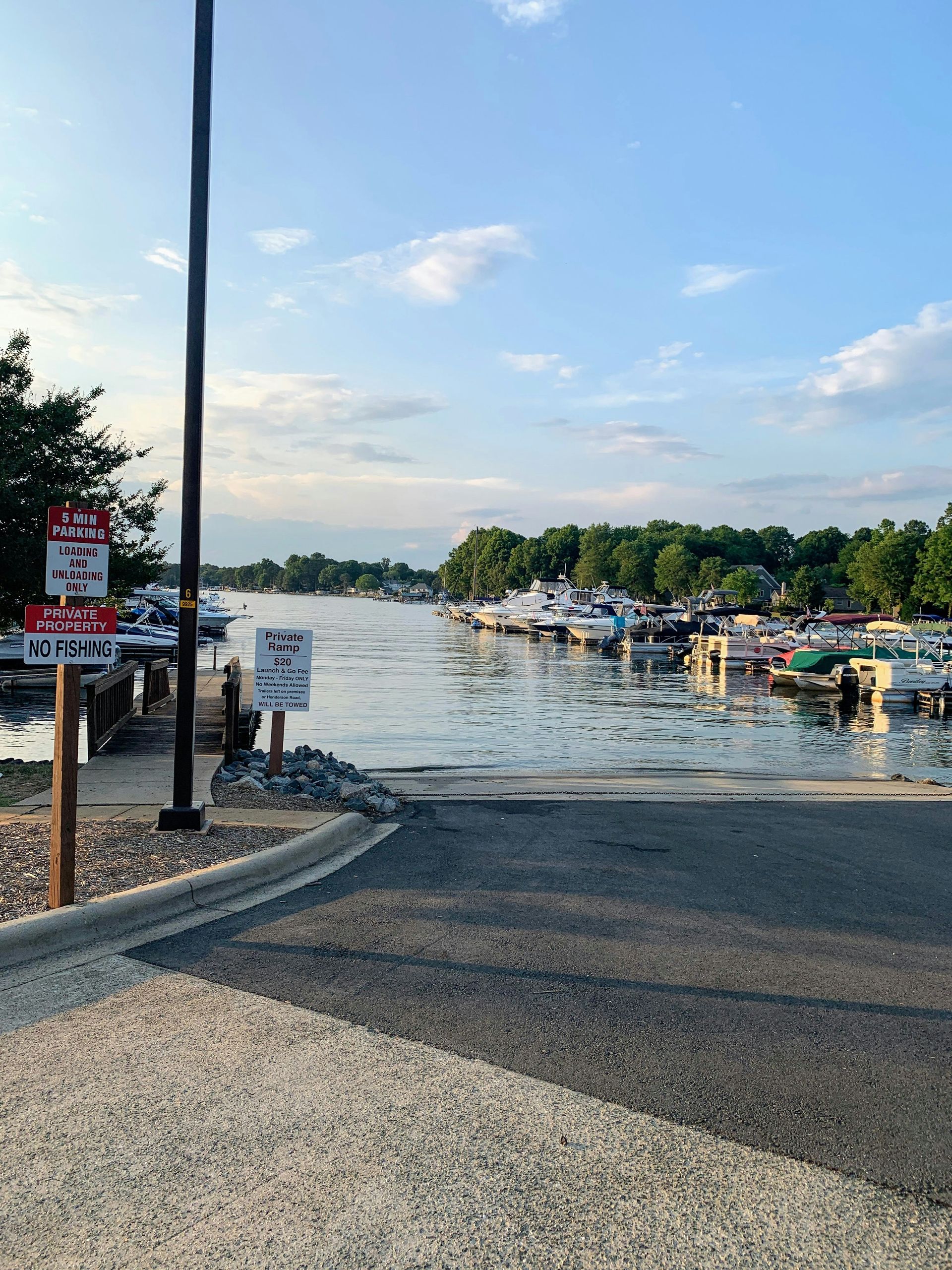 Boat ramp leading to a waterway with docked boats on either side under a partly cloudy sky.