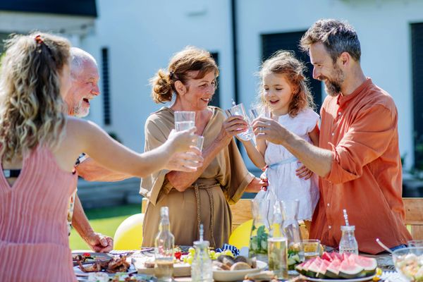 Family toasting outdoors at a table set with food. People are smiling and enjoying themselves.