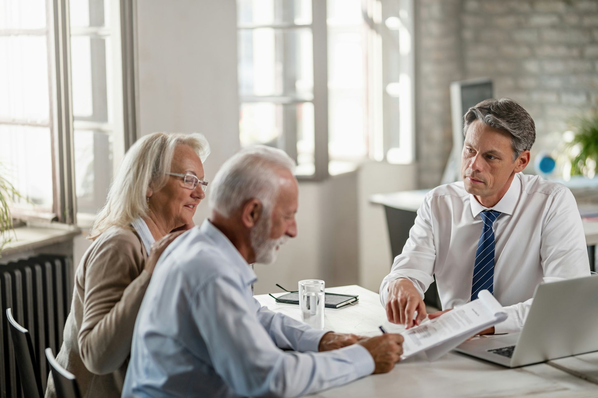 Senior couple signing documents with a financial advisor at a desk.