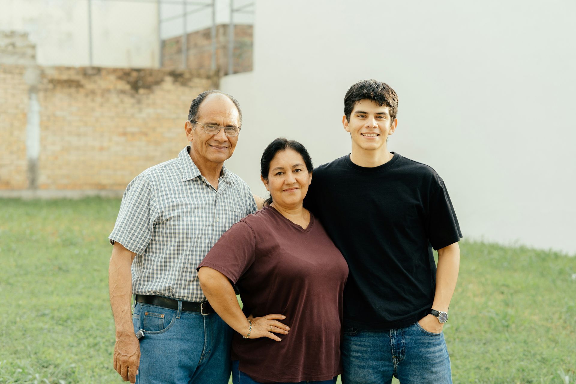 Family of three smiling outside: an older man, a woman with her hand on hip, and a teenage boy.