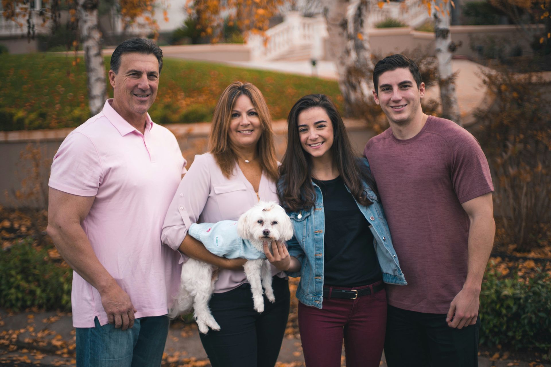 Family of four with a small dog posing outdoors in front of a home.