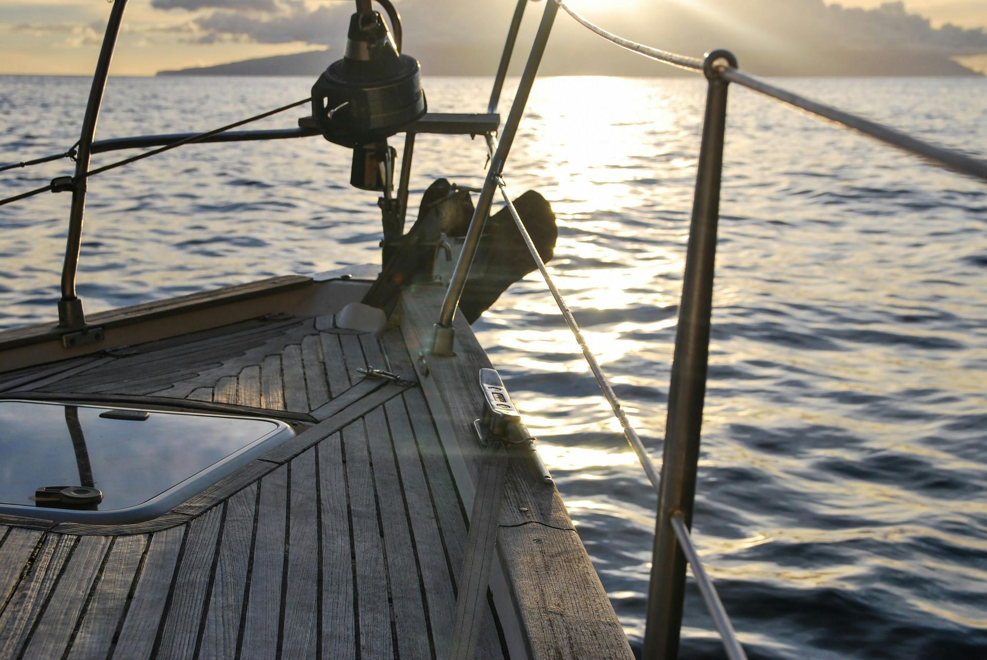 Sailboat deck at sunset, with ocean and distant island.