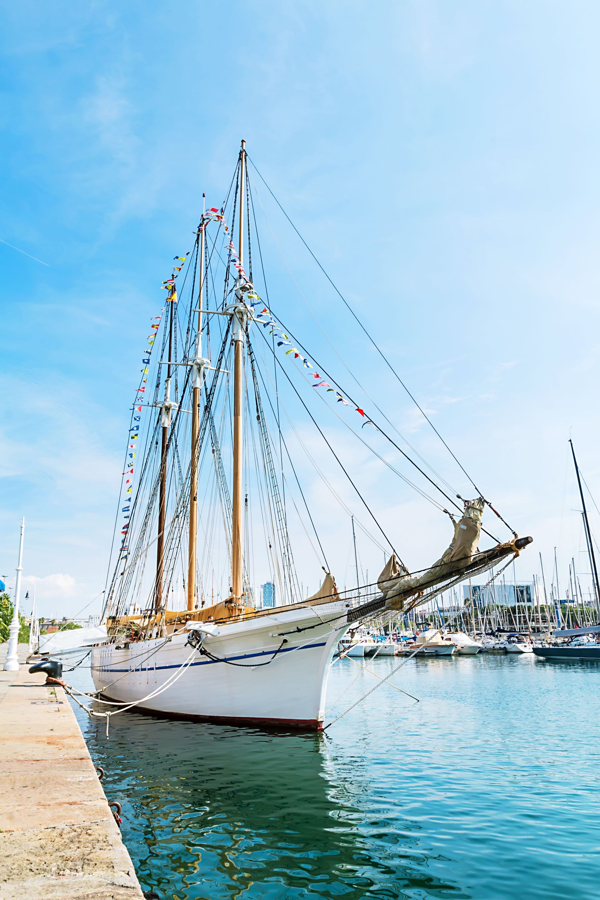 Sailboat docked at pier in harbor, under a bright blue sky.
