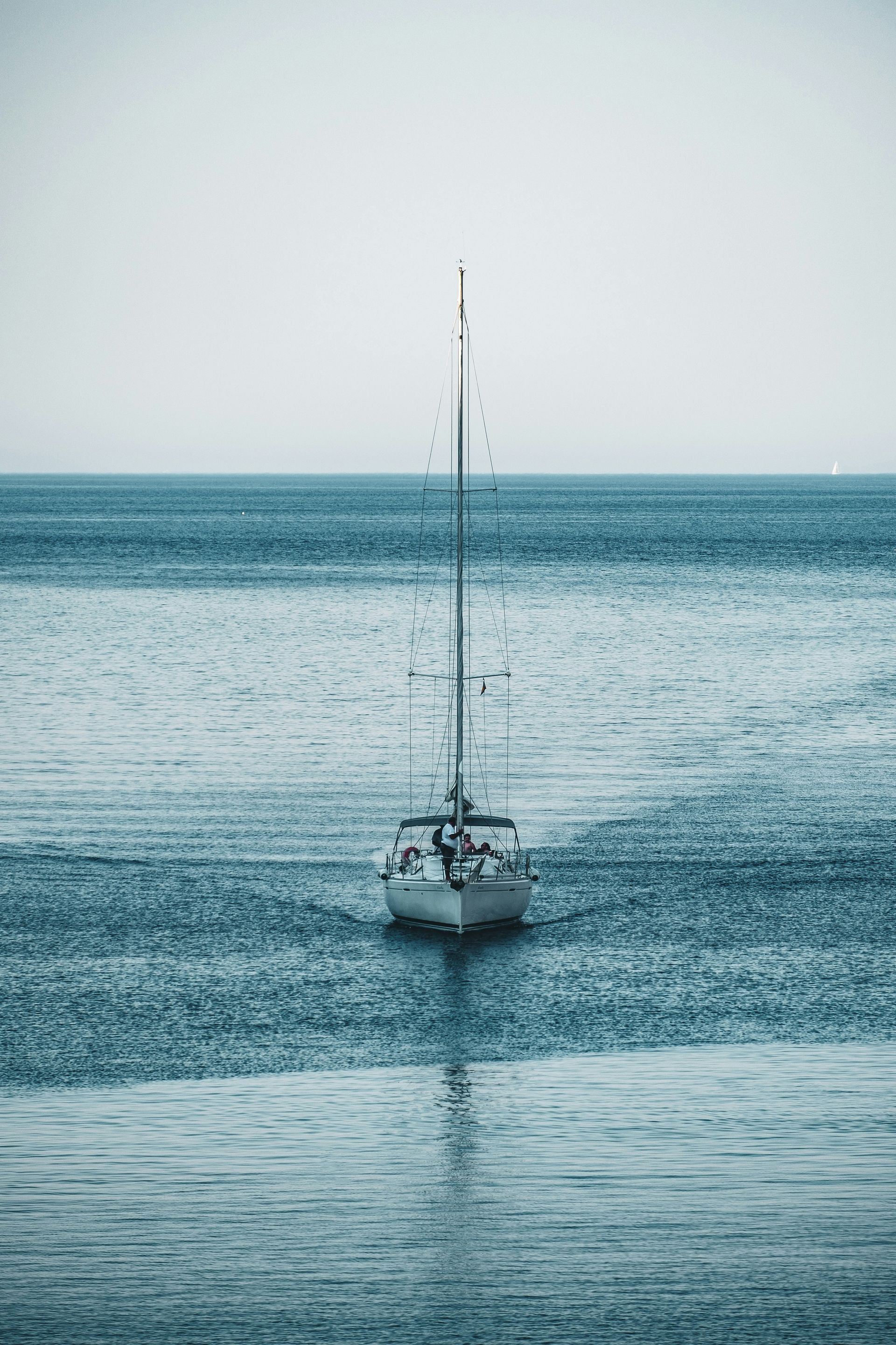 Sailboat on calm, teal-colored water, under a muted sky.