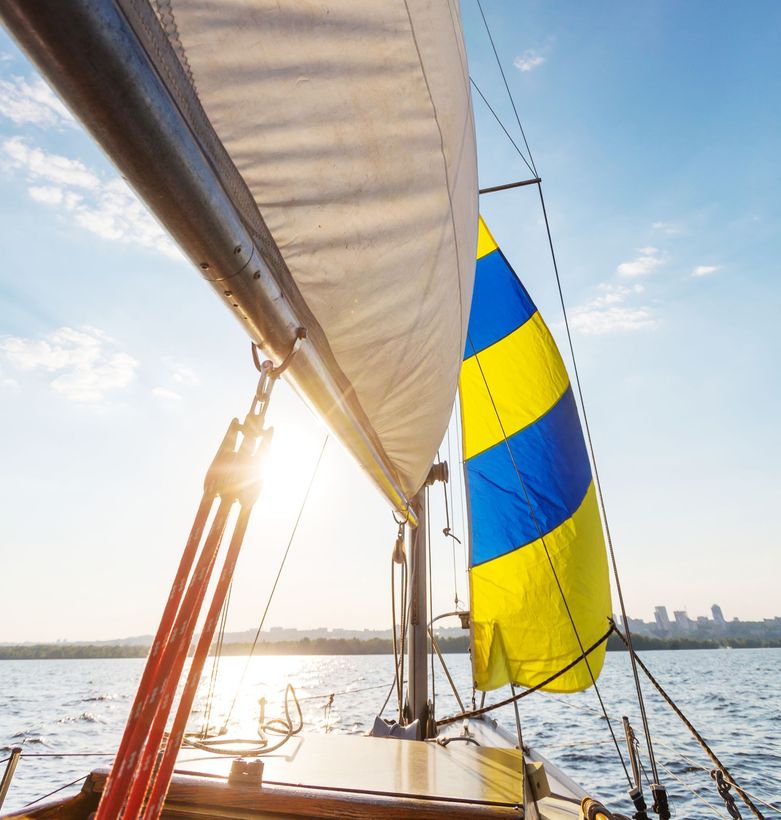 Sailboat sailing on water with blue and yellow striped spinnaker under a sunny sky.