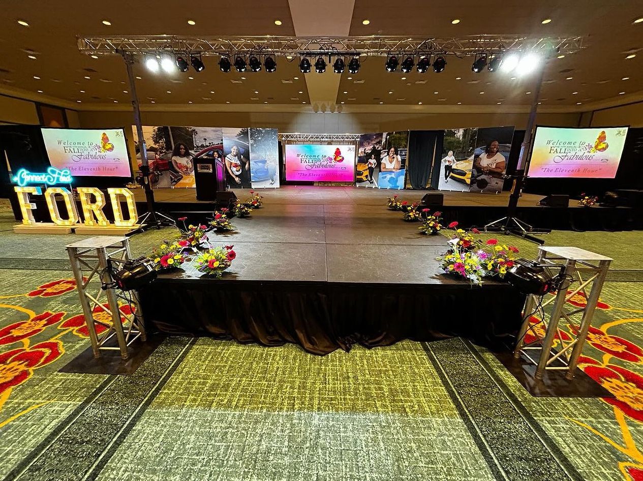A large indoor event stage decorated with flowers, lit marquee letters spelling 