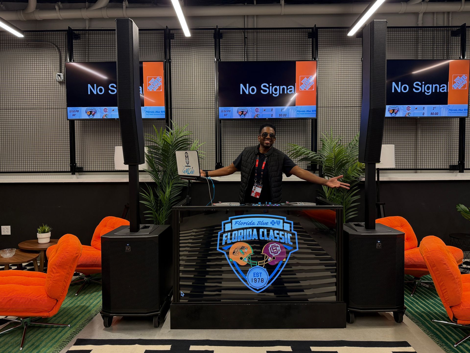 A smiling DJ stands behind a Florida Classic branded booth in a lounge with orange chairs and black tower speakers.