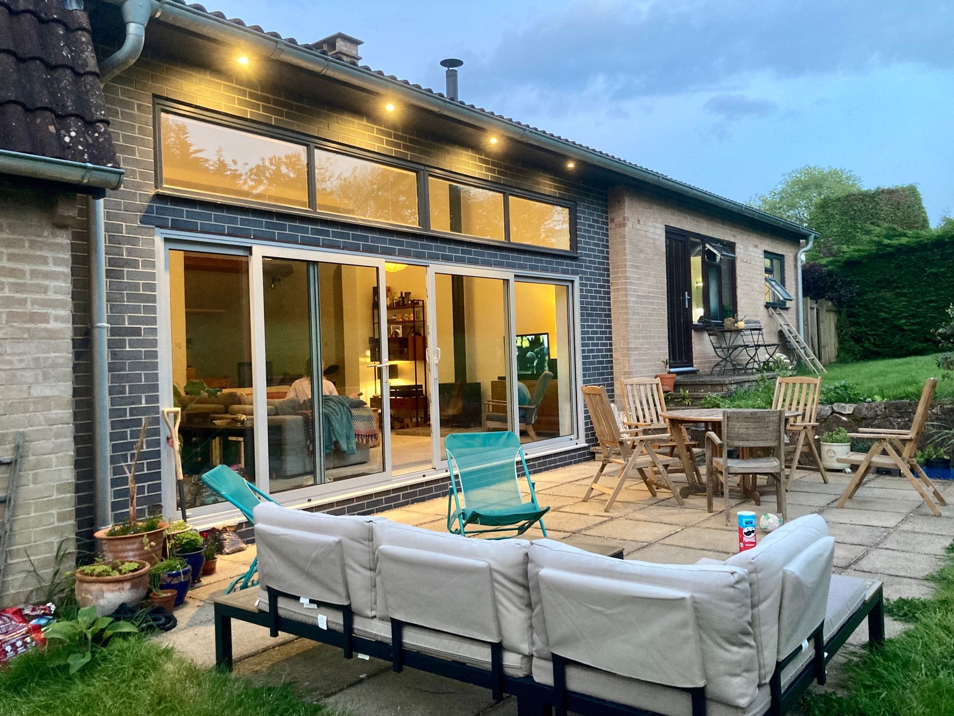 A patio with a couch and chairs in front of a house with outside lighting.