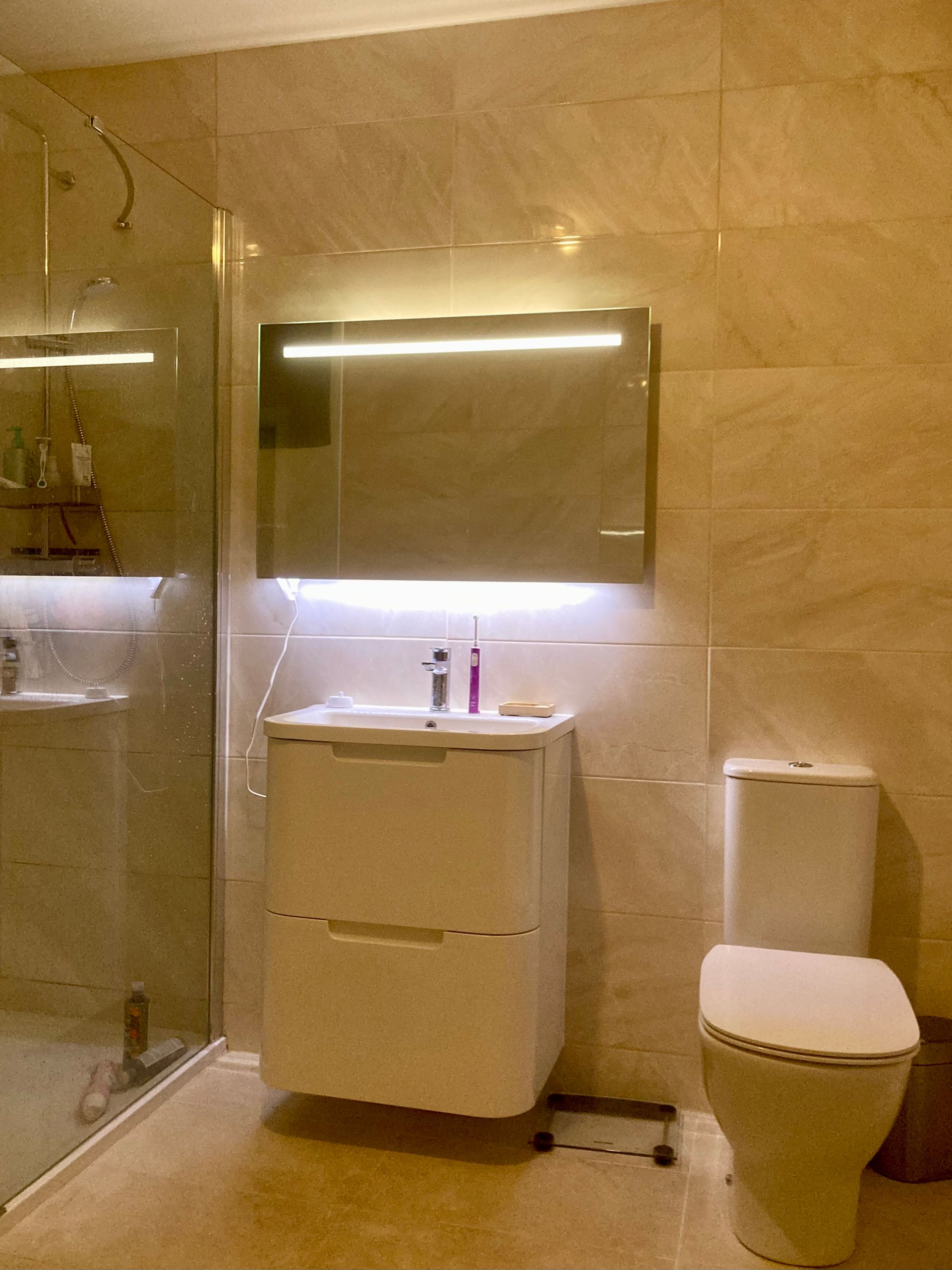 A bathroom with a toilet , sink , mirror and shower.