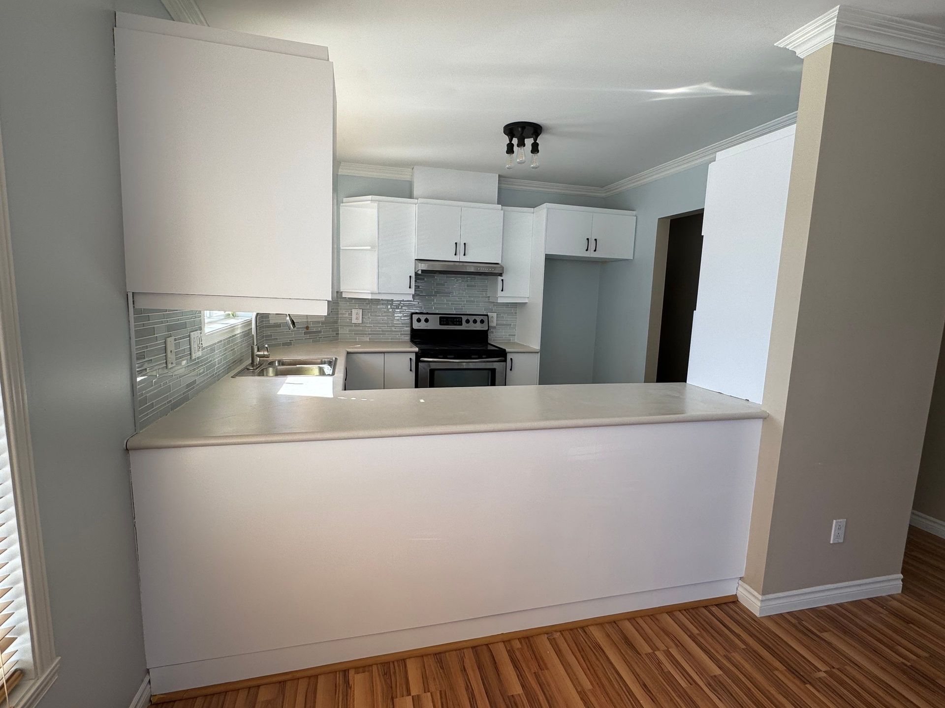 Cuisine blanche avec comptoir, armoires, électroménagers et planchers de bois.