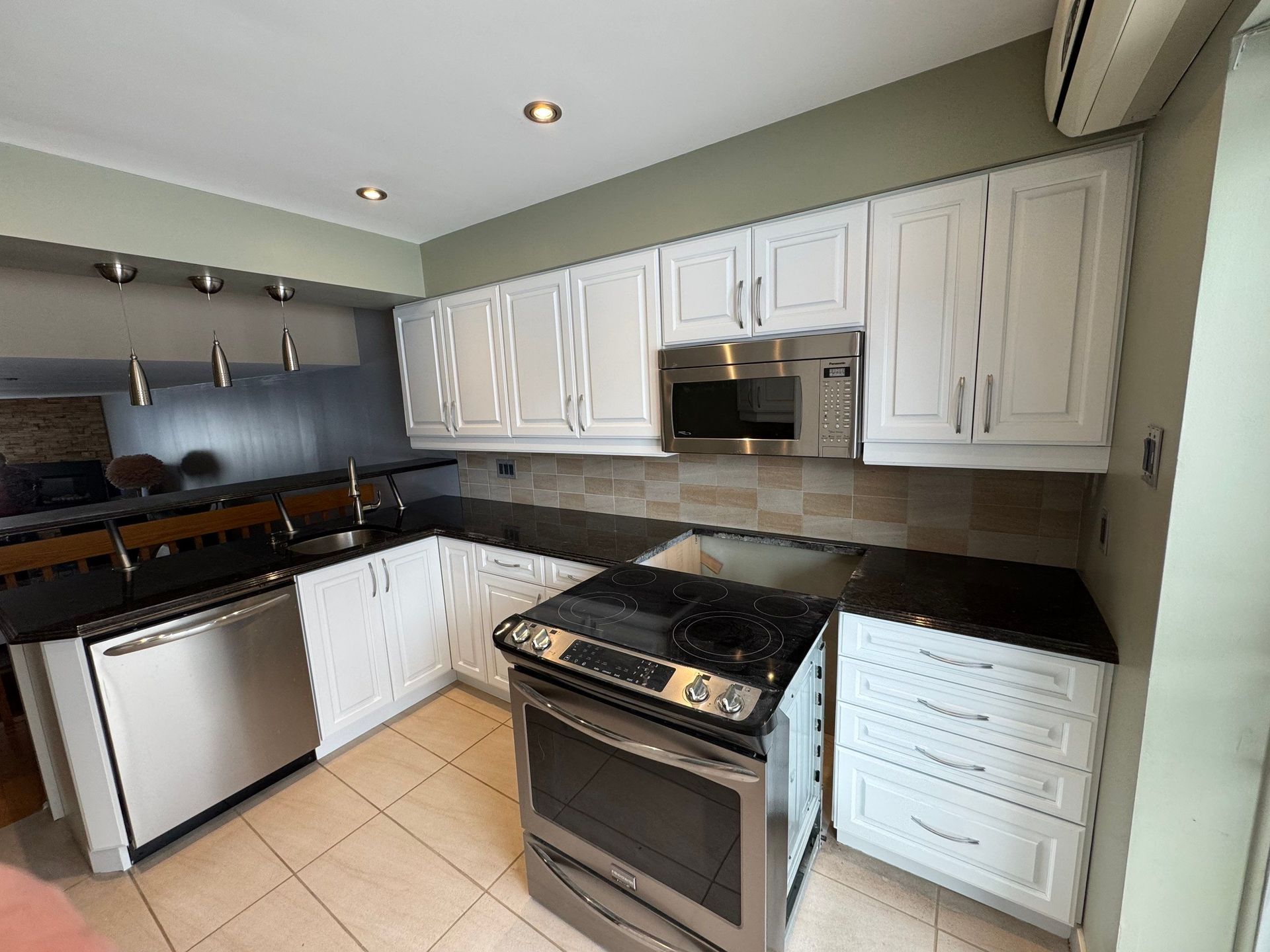 Une cuisine blanche avec des comptoirs noirs et des appareils en acier inoxydable.