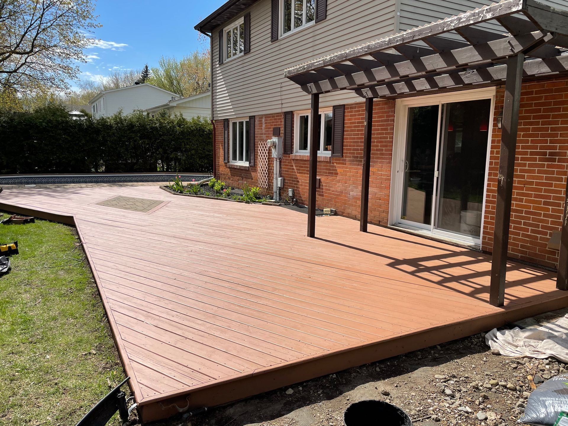 Une terrasse en bois avec une pergola, attachée à une maison en briques, entourée d'herbe.