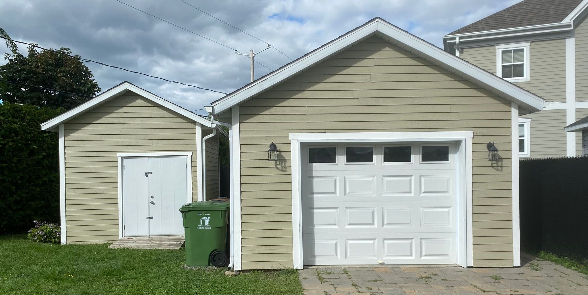 Deux bâtiments beiges, l'un avec une porte de garage et l'autre avec une porte blanche, se dressent l'un à côté de l'autre.