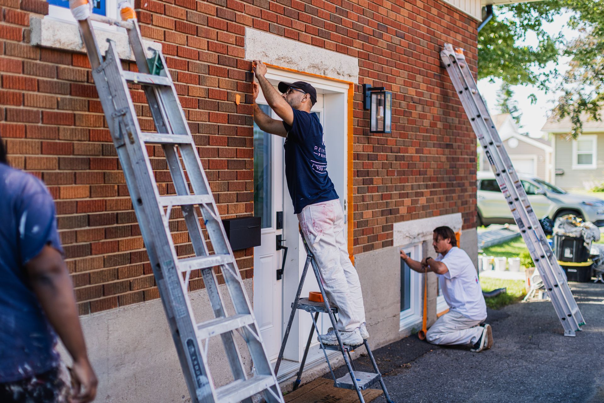 Deux hommes peignent un bâtiment en briques avec des échelles.
