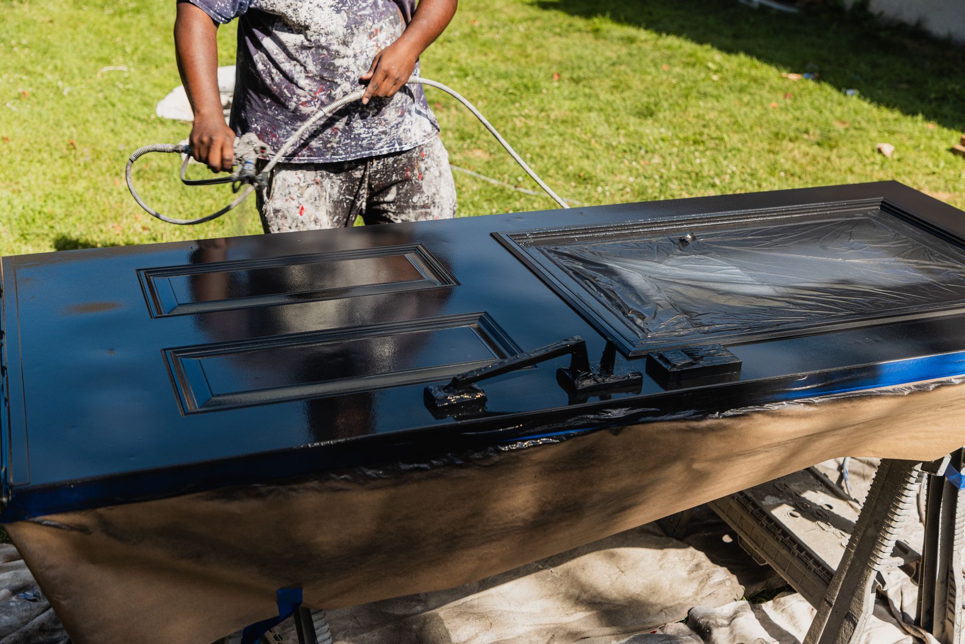 Un homme peint une porte noire avec un tuyau.