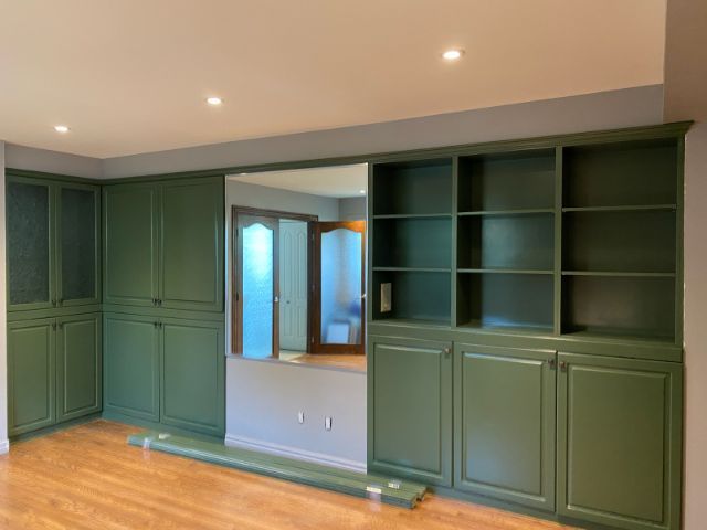 Des placards intégrés verts avec étagères ouvertes et rangements fermés, un parquet et un miroir dans une pièce.