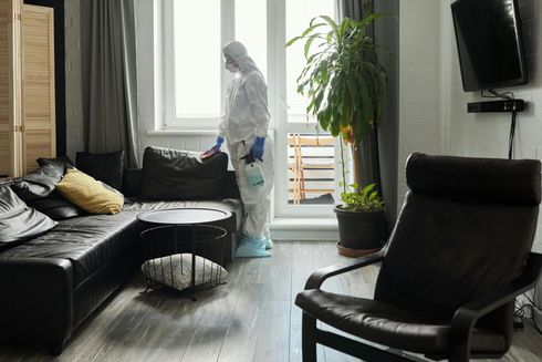 A man in a protective suit is disinfecting a living room.