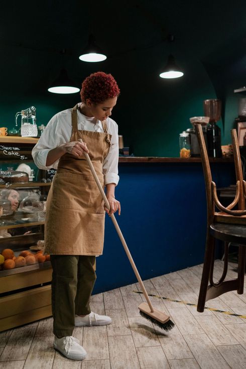 A woman is sweeping the floor in a restaurant with a broom.
