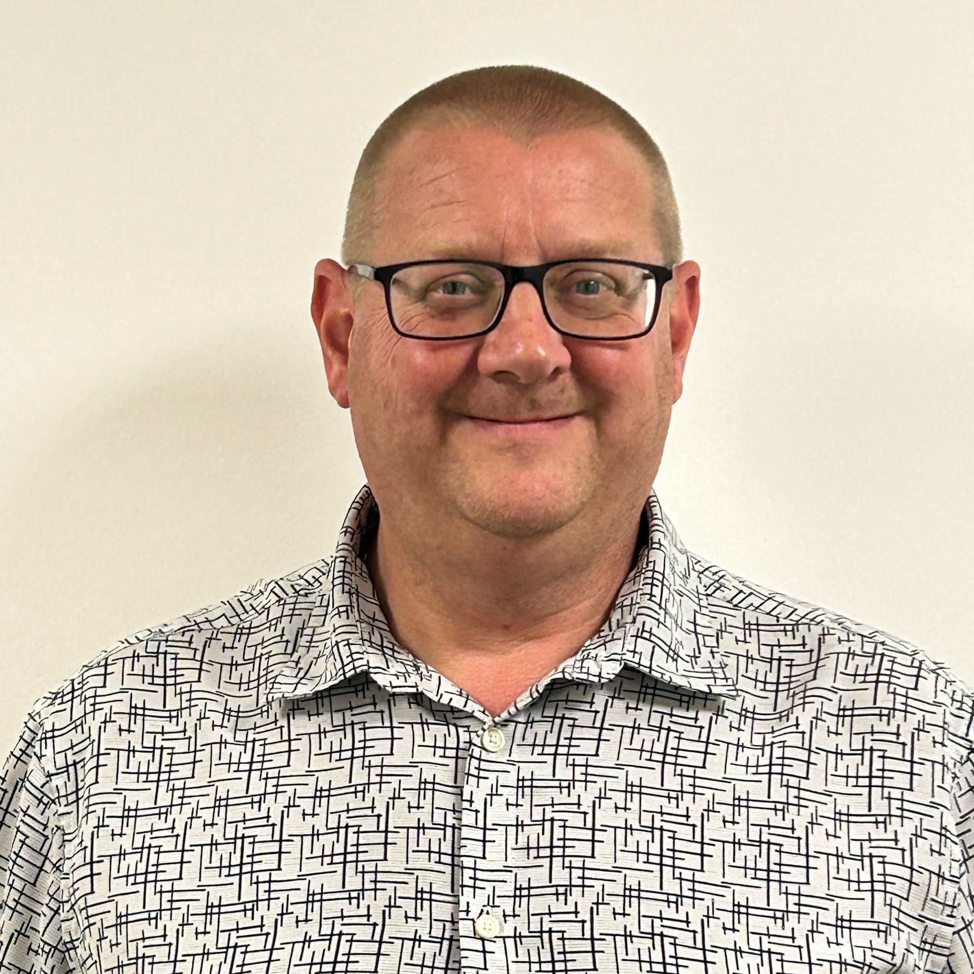 A man wearing glasses and a patterned shirt is smiling for the camera.