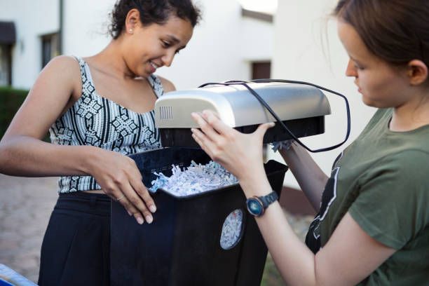 Women emptying shredded paper from shredder bin for secure paper shredding services outdoors.