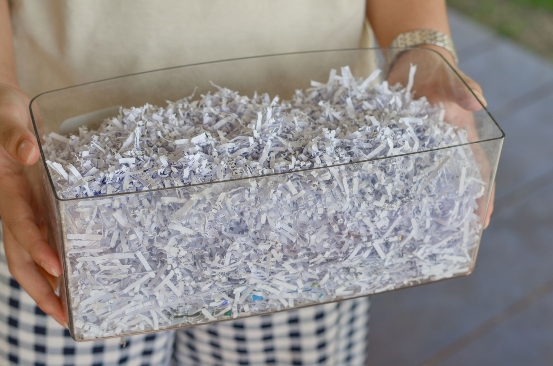 A person is holding a transparent container of shredded paper.