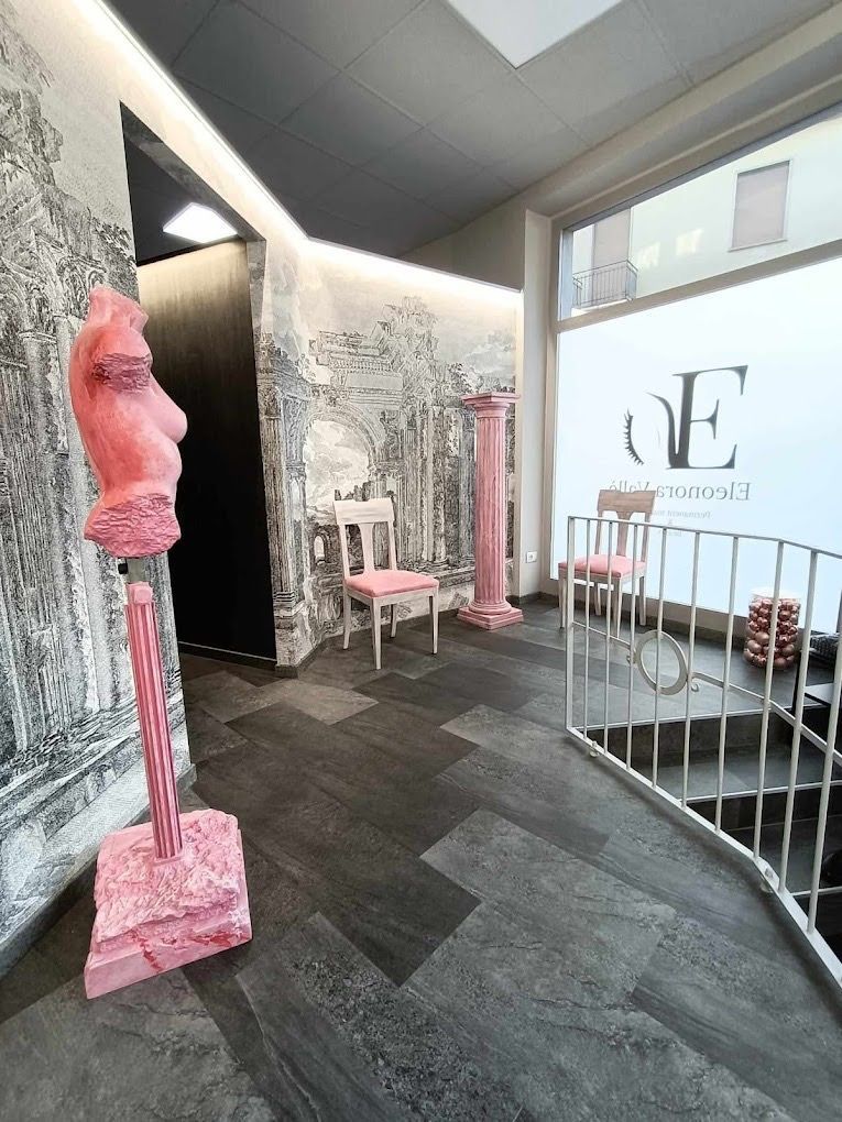 Testa scultorea rosa esposta in uno spazio espositivo moderno con posti a sedere e una grande finestra.